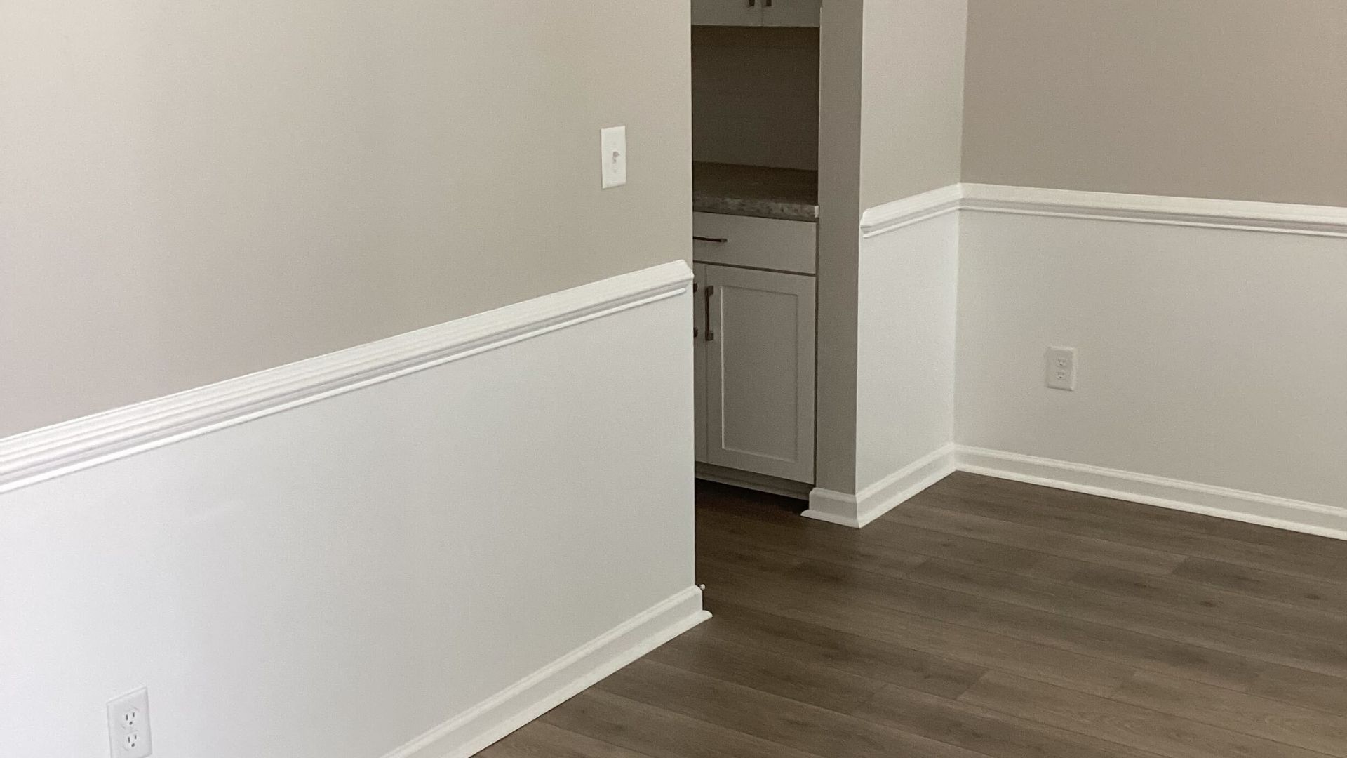 Interior view of a dining room with white wainscoting and neutral paint.
