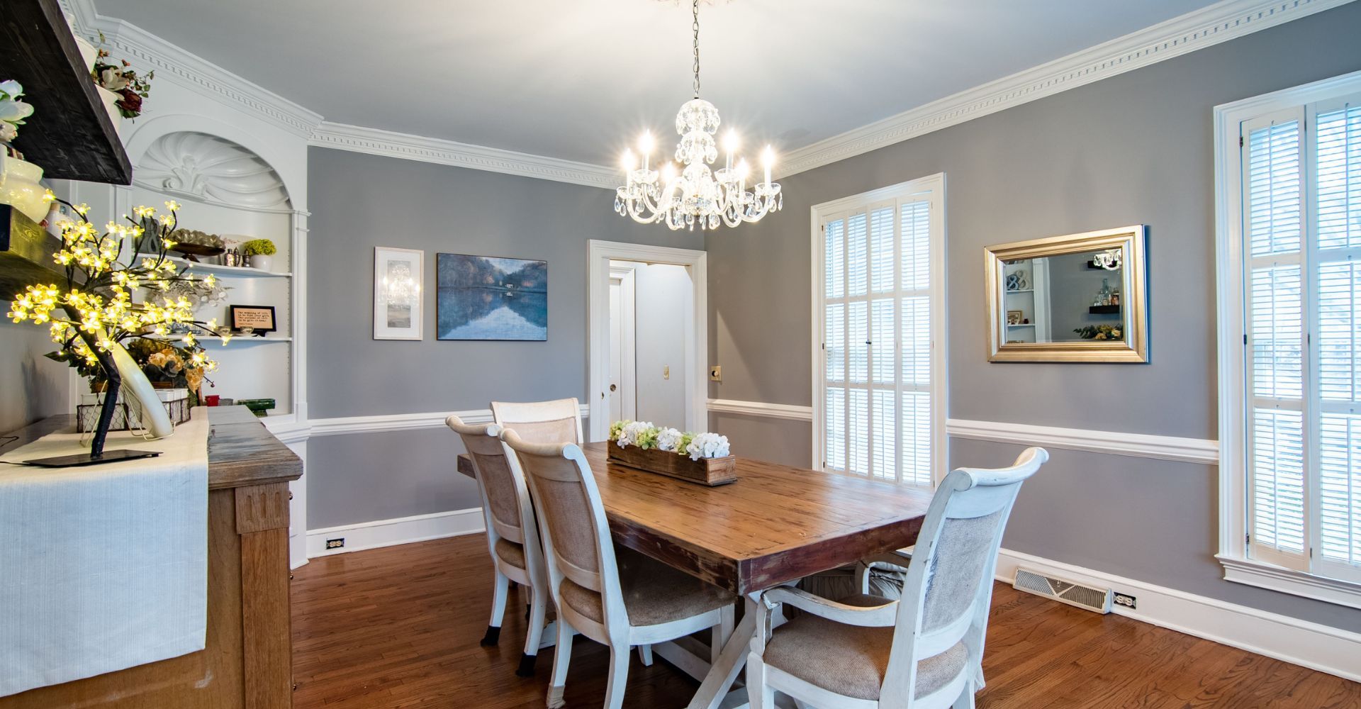 Elegant dining room with gray walls, crystal chandelier, and wooden table.