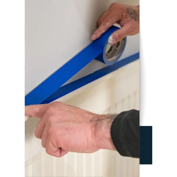 Easley (1) Painter's hands applying blue painter's tape to a wall edge.