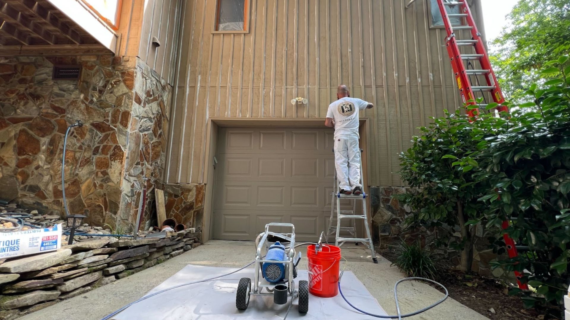 Painter spraying siding on house, prepping for exterior paint job