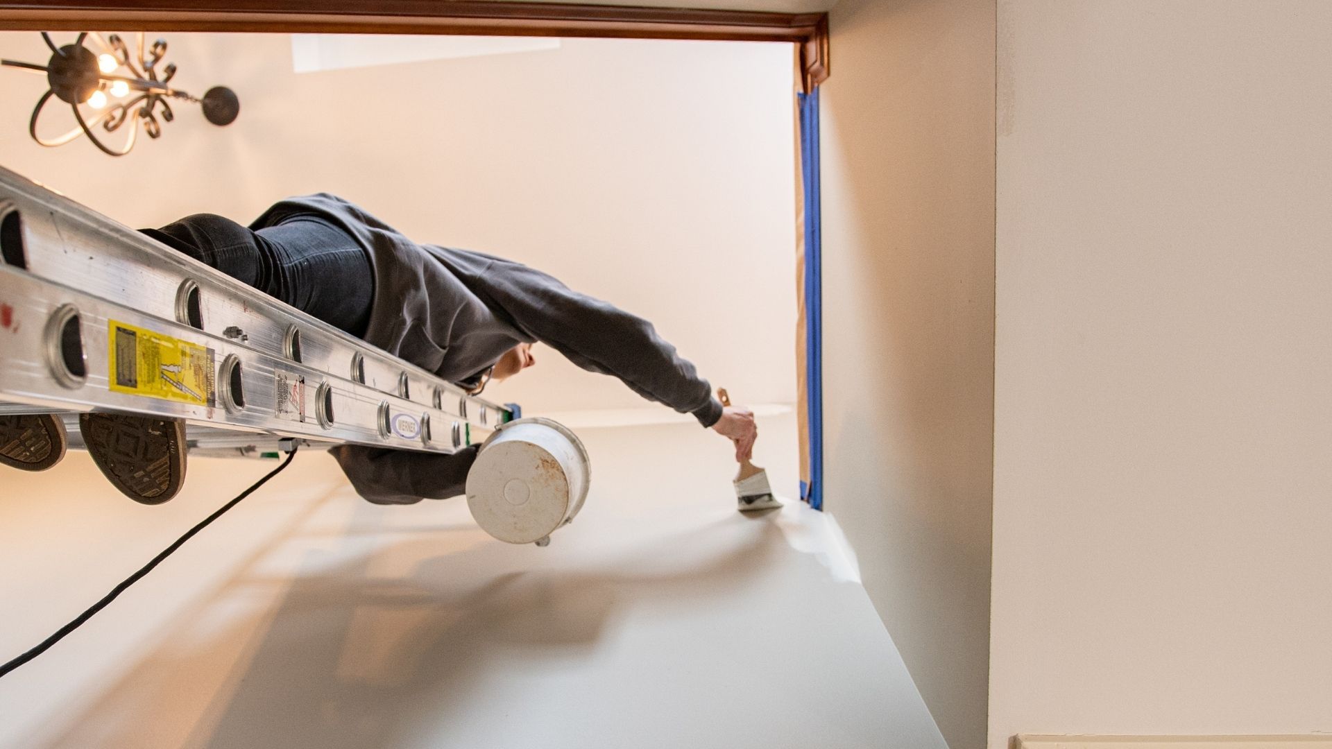 Painter on ladder, painting wall, checking for contractor license and insurance.