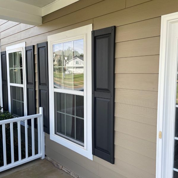 HowCanIKeepPaintFromDryingOut-2 Exterior house siding with tan color, black shutters, and white trim windows.