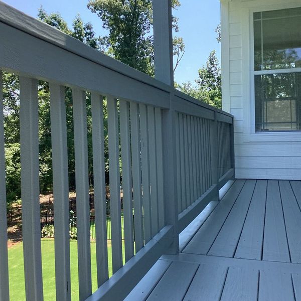 HowCanIKeepPaintFromDryingOut-4 Gray painted deck railing and floorboards on a sunny day with trees in the background.