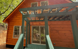 Portfolio 299 Orange log cabin with green deck and pergola, nestled in trees