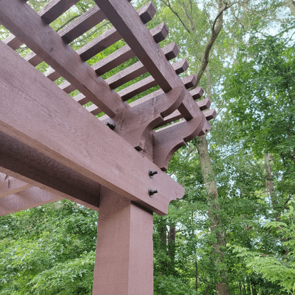Professional Staining PB CTA Images 29 Brown stained pergola detail with fasteners and lush green trees in background.