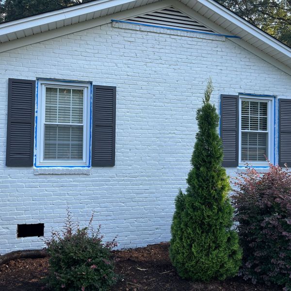 What Colors Last the Longest on Exteriors-image1 White brick house exterior with dark shutters and blue painter's tape around windows.