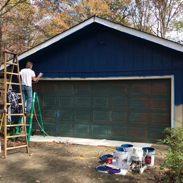 What Is Causing My Paint To Fade and Peel-img2 Man painting a dark blue garage door, showing paint fading and peeling.