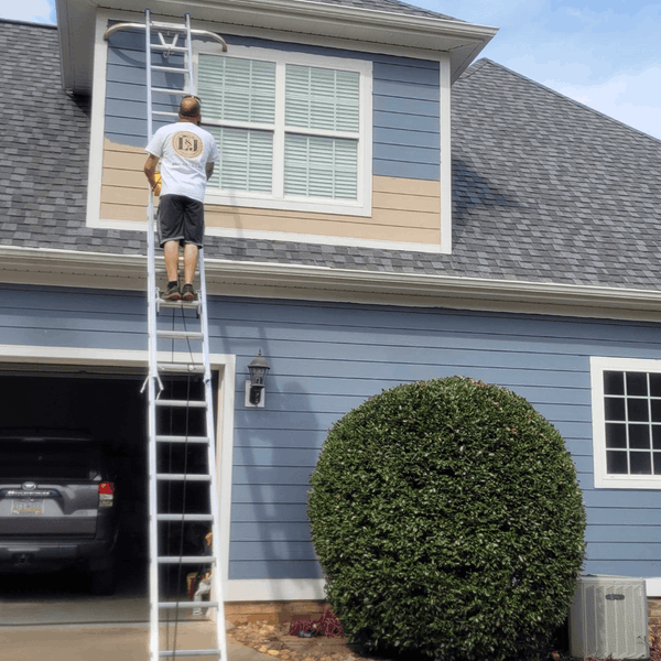 Man painting exterior siding on a house with a ladder