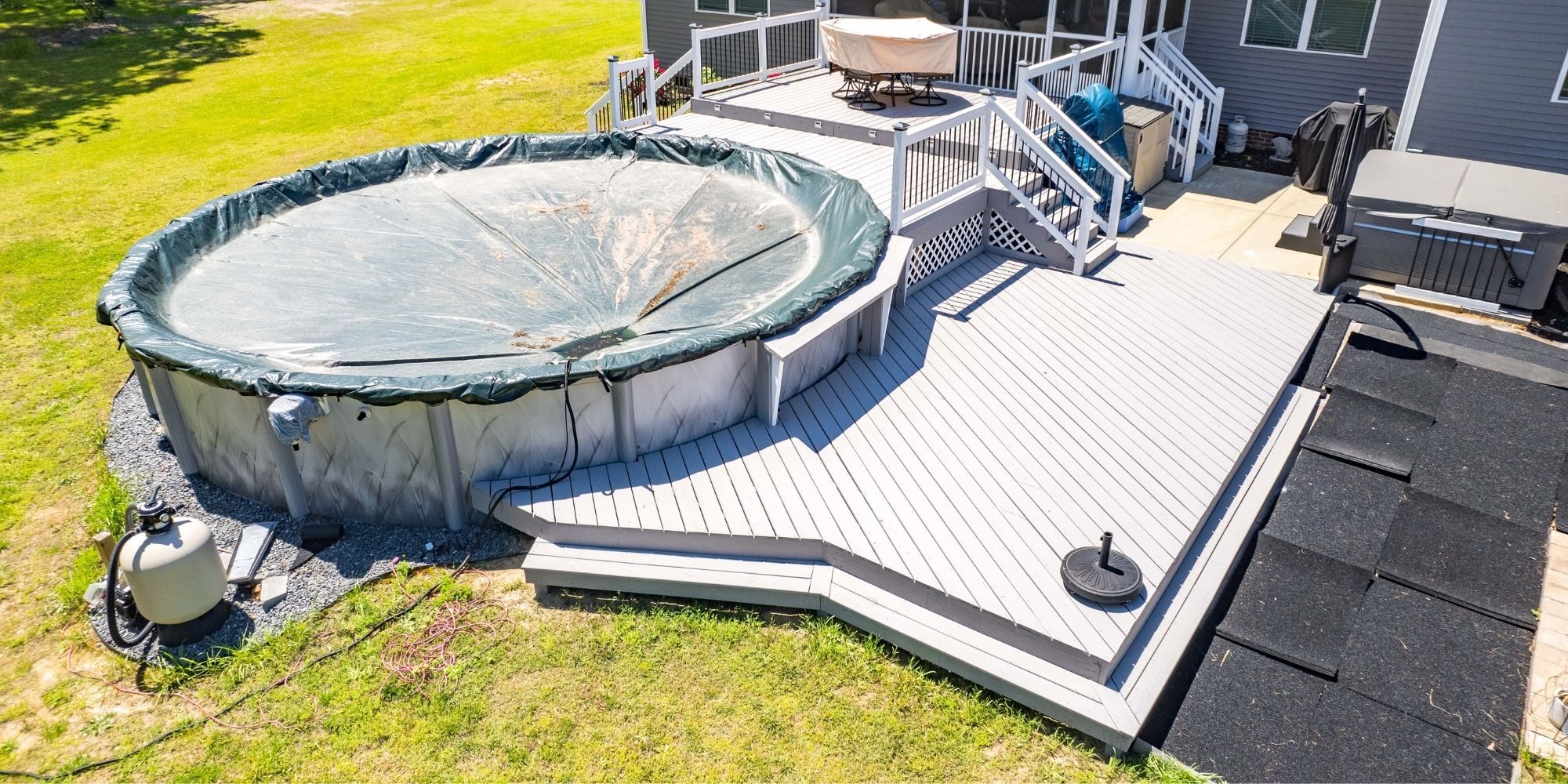 Peeling paint on a gray deck with an above-ground pool and hot tub.