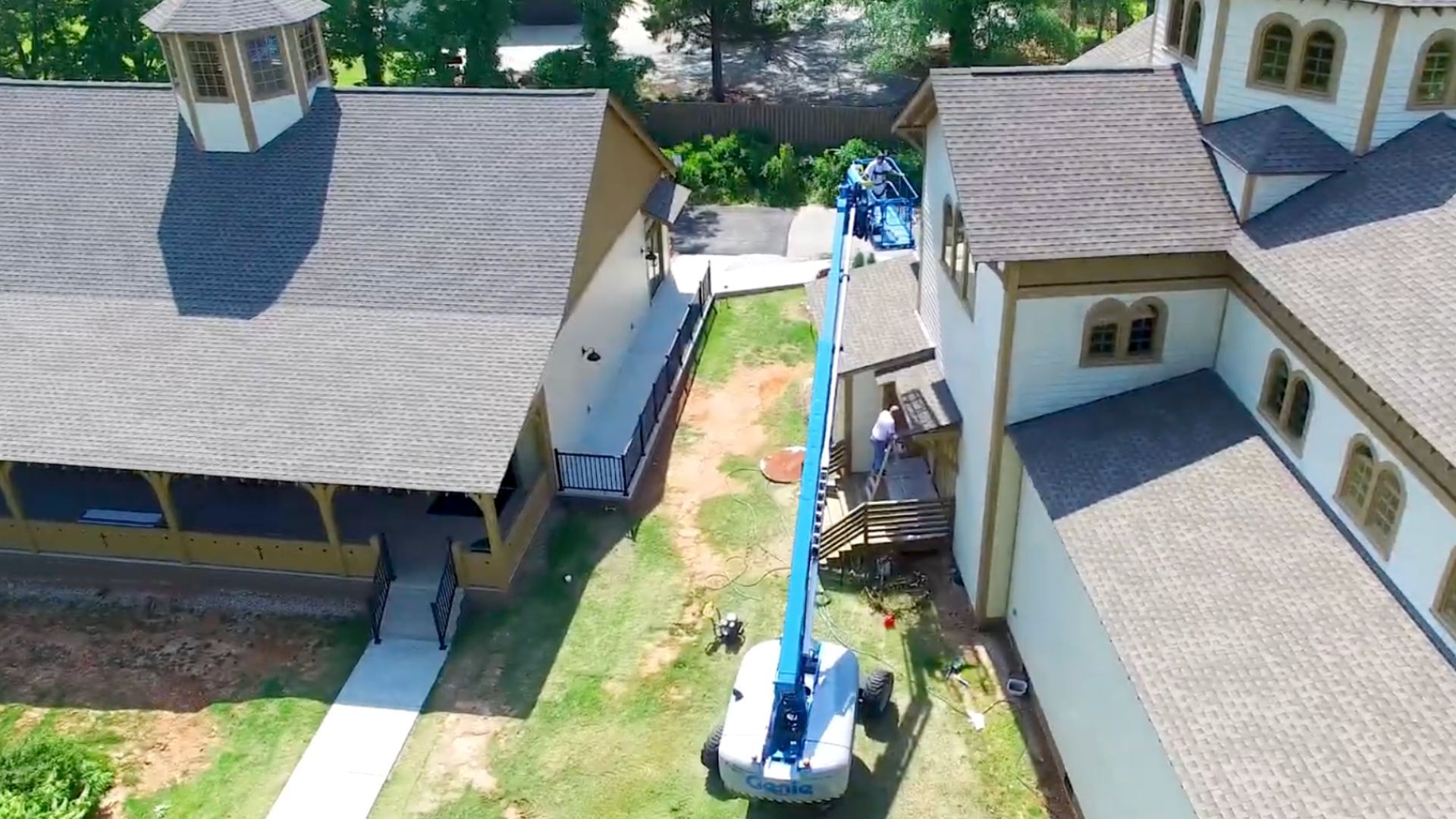Workers in a boom lift paint the exterior of a tan commercial building.