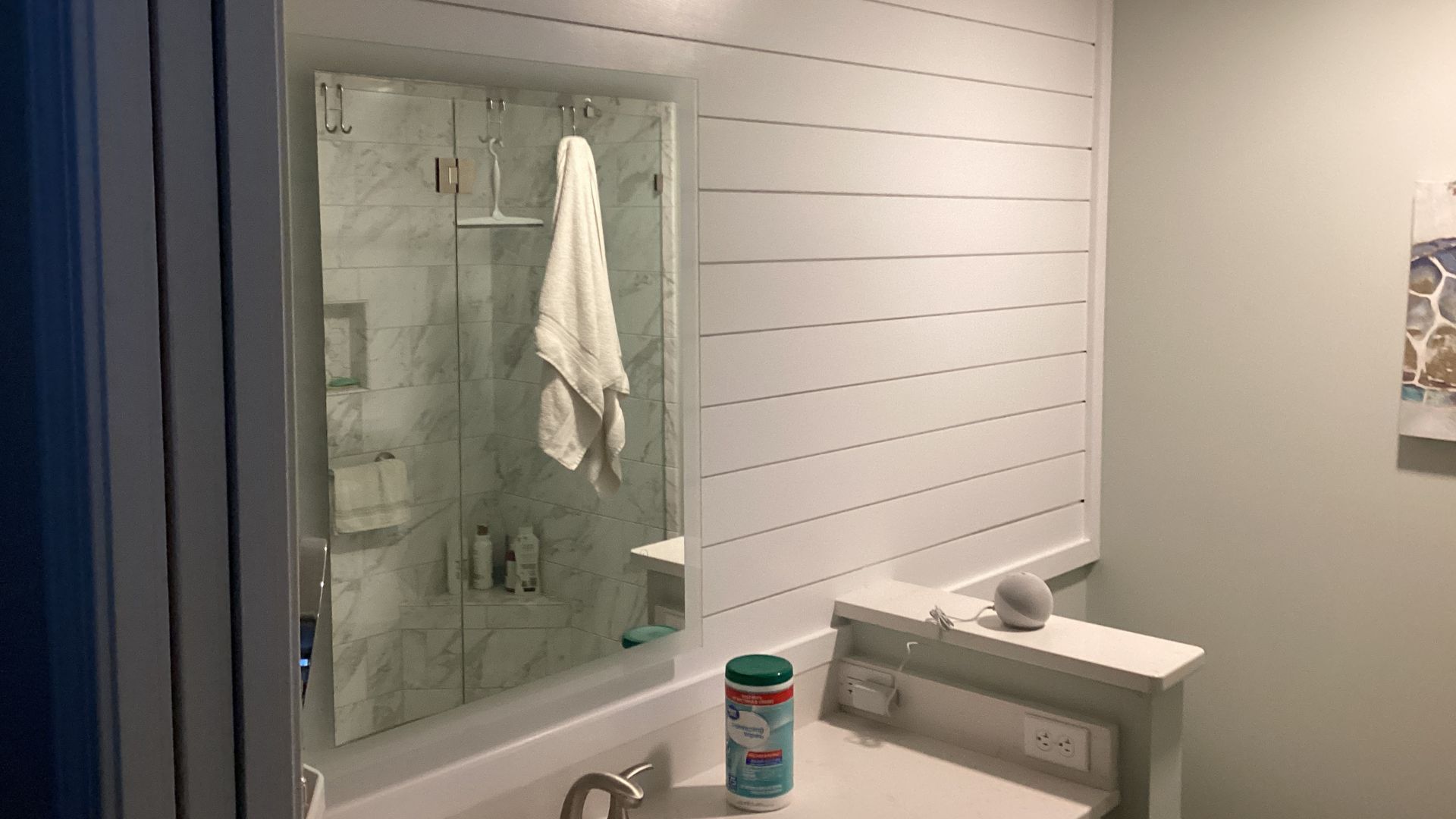 Modern bathroom with shiplap wall, mirror reflecting shower, and countertop items.