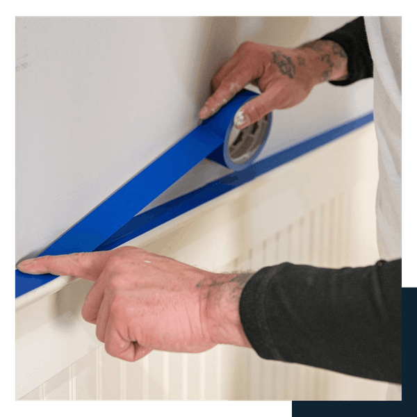 careers 291 Person applying blue painter’s tape along the edge of a wall, preparing for painting.