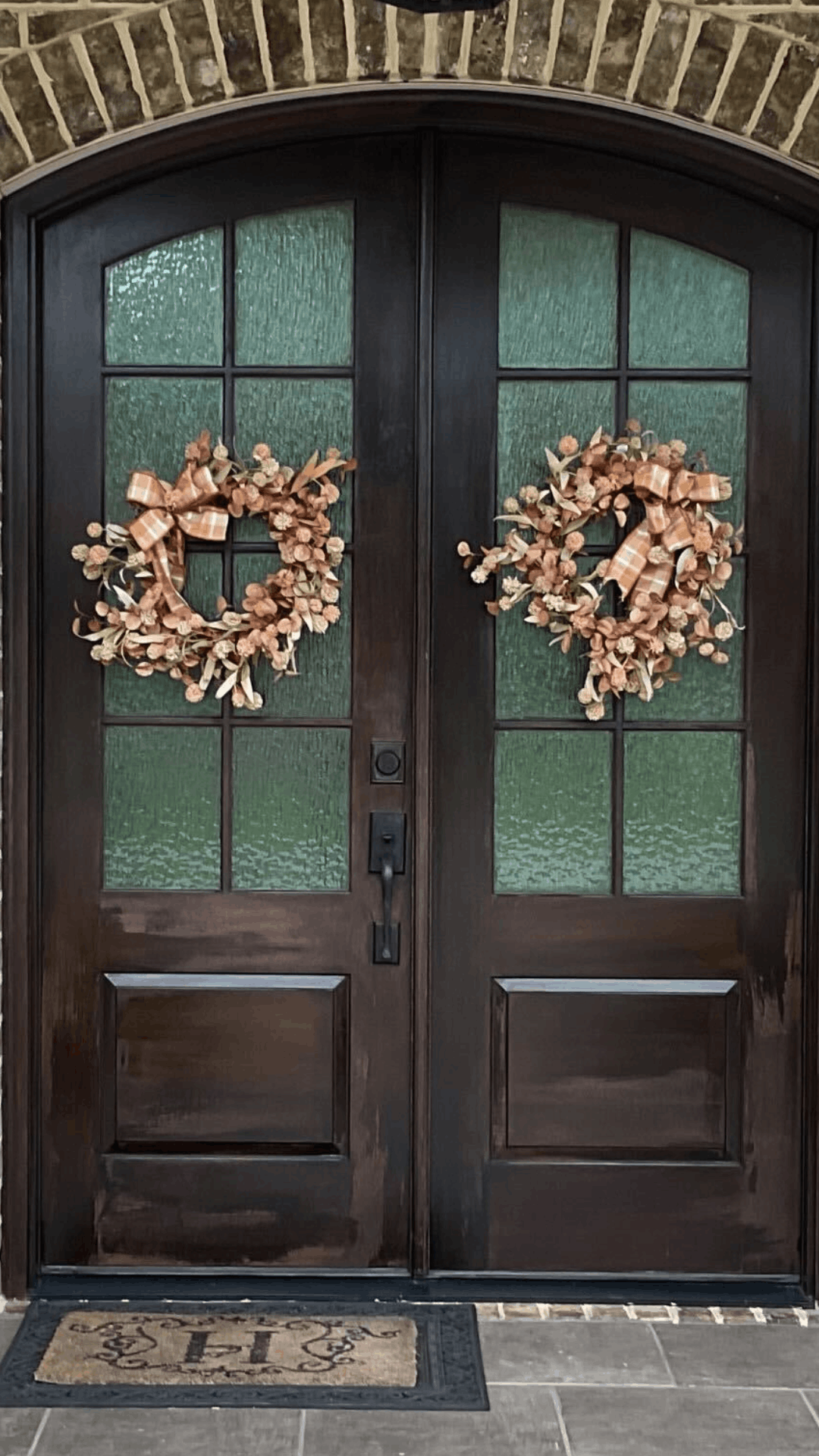 Dark stained double front doors with glass panes and autumn wreaths