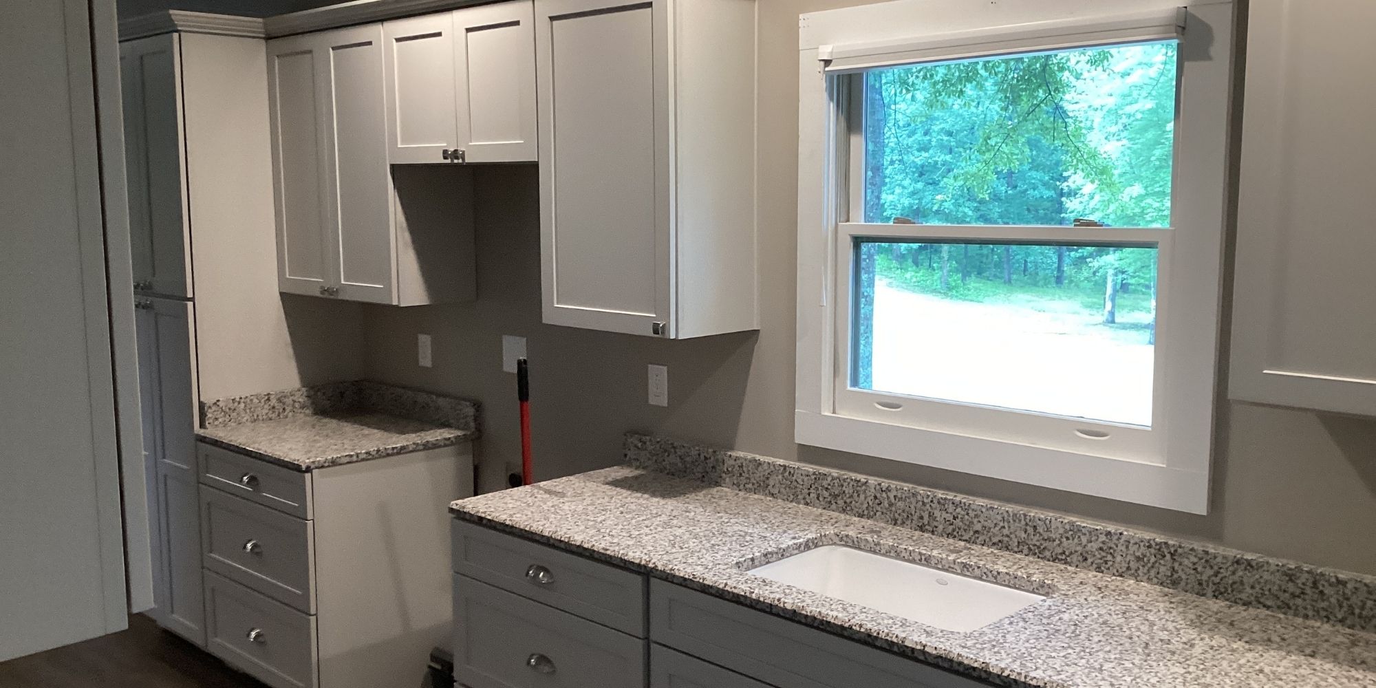 Newly painted kitchen cabinets in a light gray with granite countertops and a sink.