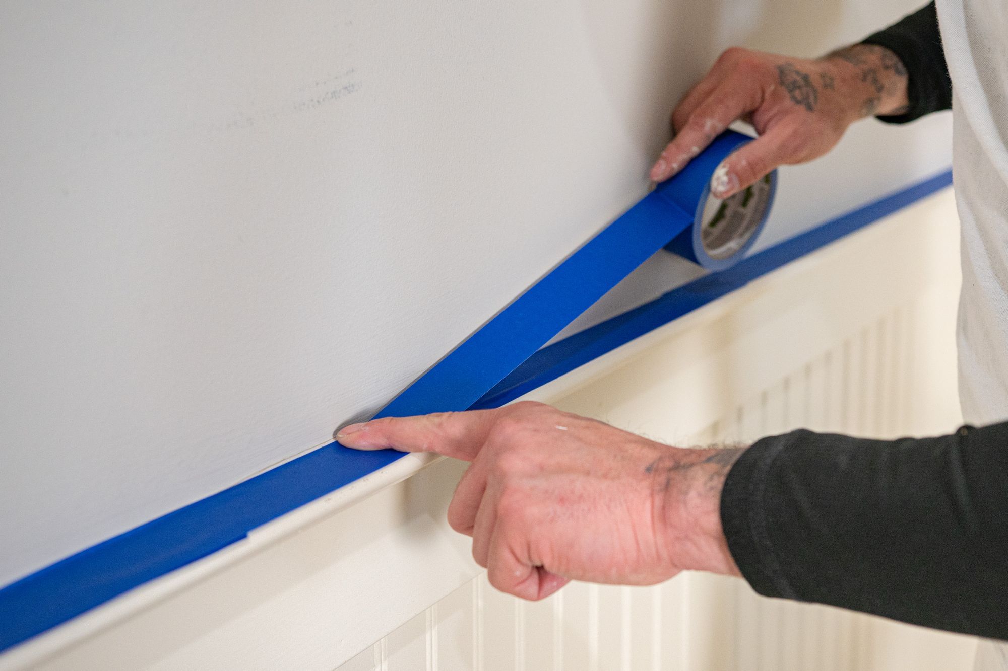 lj_painting_027 Painter applies blue painter's tape to a wall and trim for a clean paint line.