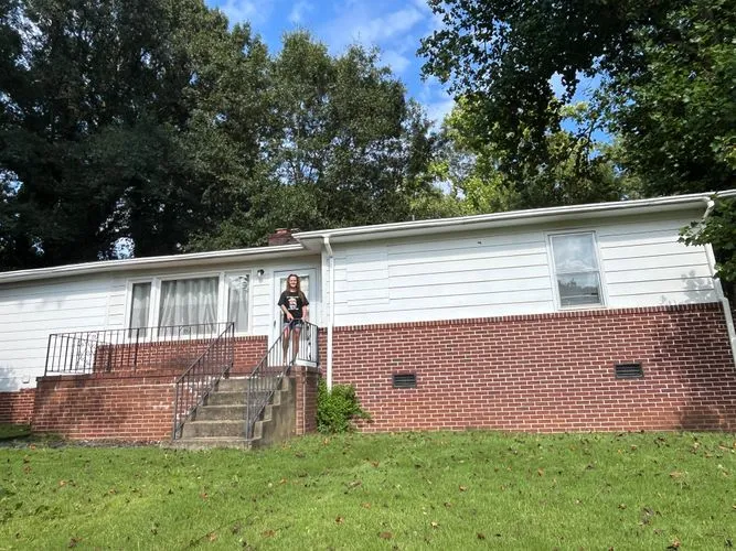 Ranch House With Brick Base And Person On Porch Kasey posing outside before renovation.
