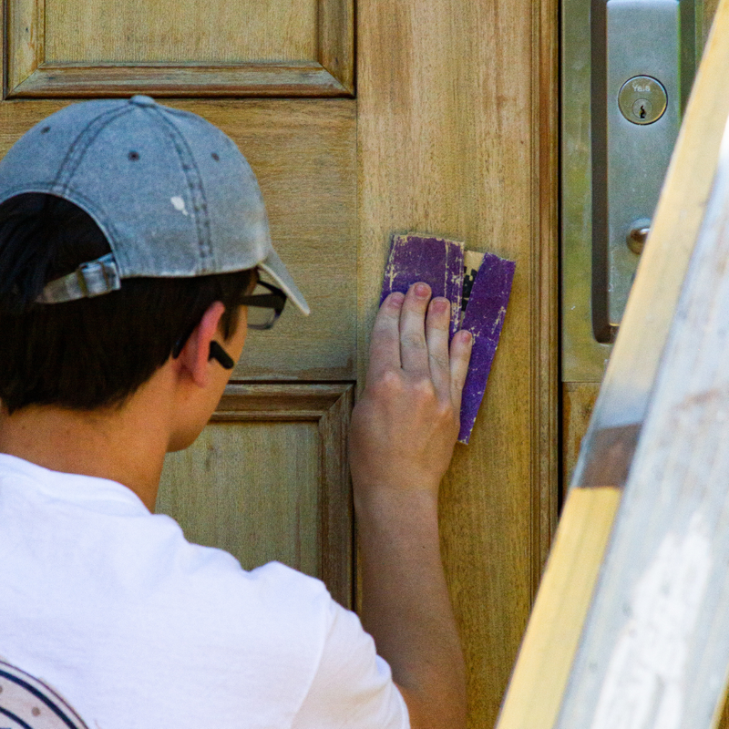 Portfolio 29 Man sanding a wooden door, preparing for refinishing.