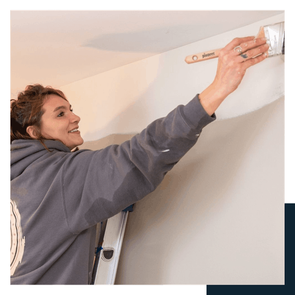 careers 29 A woman applying paint to a wall with a brush, focused on her task in a well-lit room.